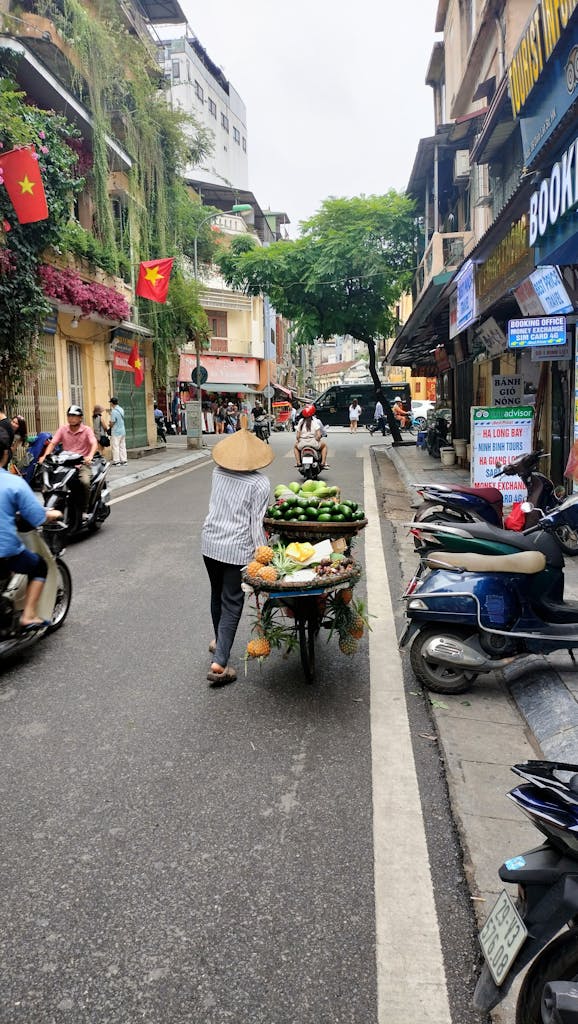 A street vendor pushes a fruit cart in Hanoi, showcasing daily life in Vietnam's bustling city streets.
