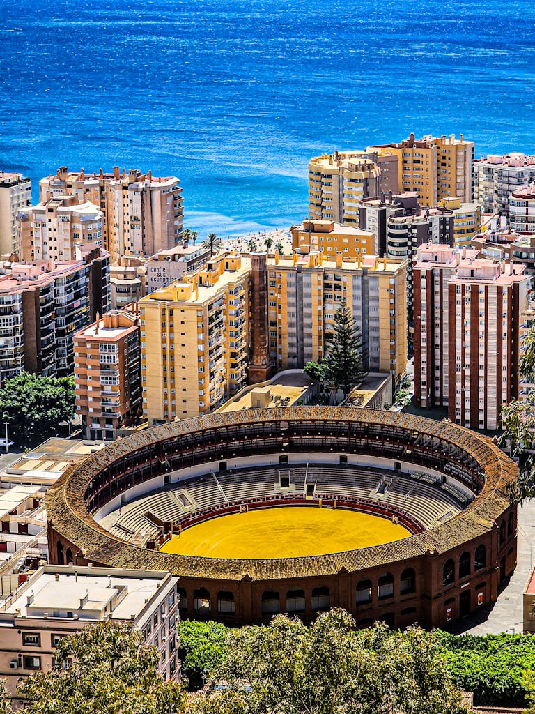 Aerial view of Málaga's Plaza de Toros and the Mediterranean Sea on a sunny day.