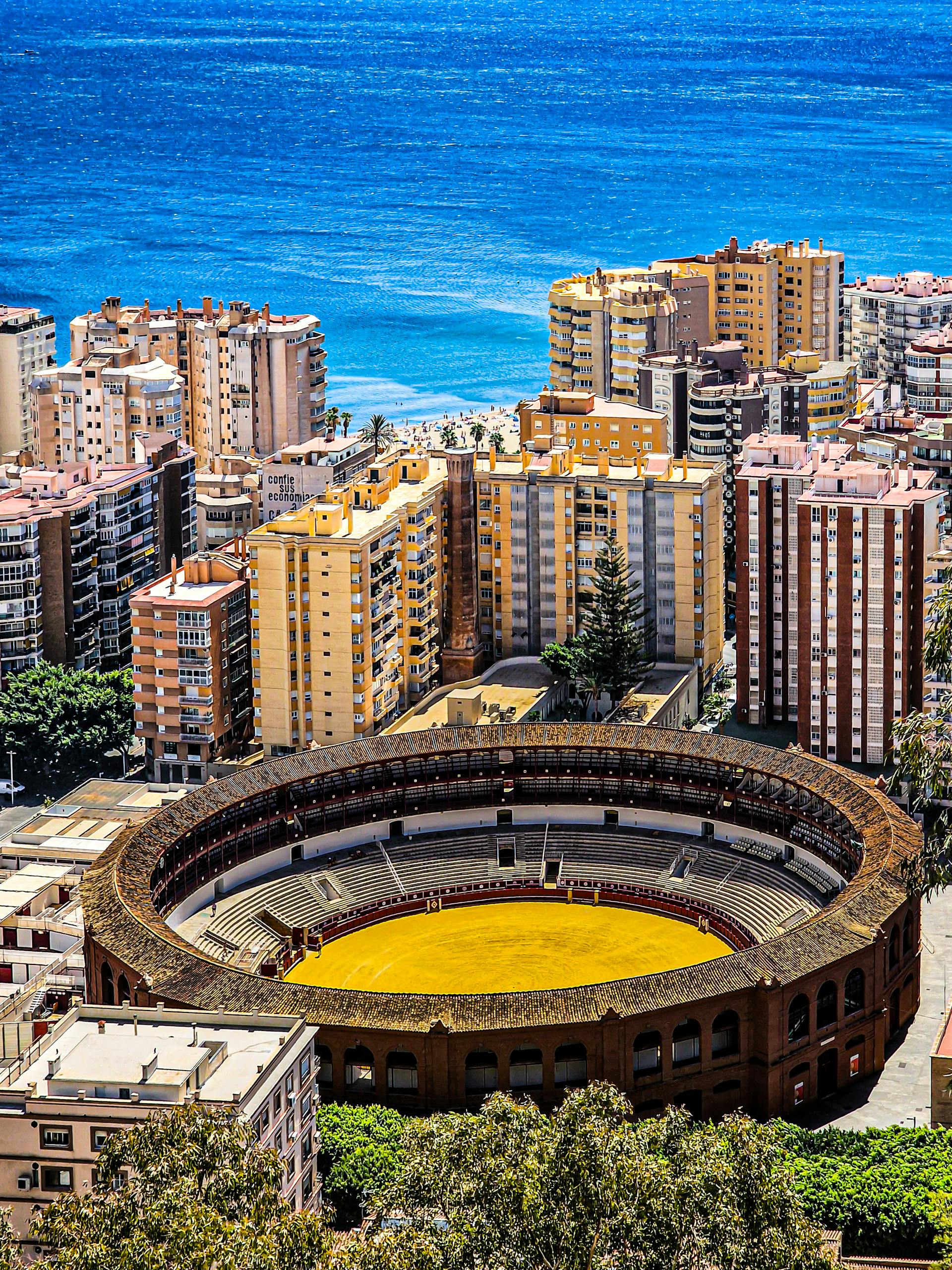 Aerial view of Málaga's Plaza de Toros and the Mediterranean Sea on a sunny day.