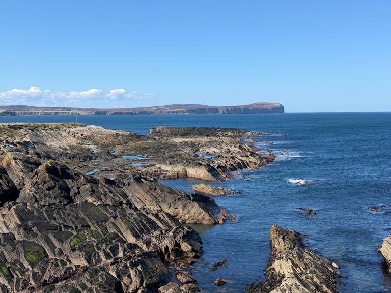 Stunning seascape along the rugged coast of the Orkney Islands, Scotland, under a clear blue sky.