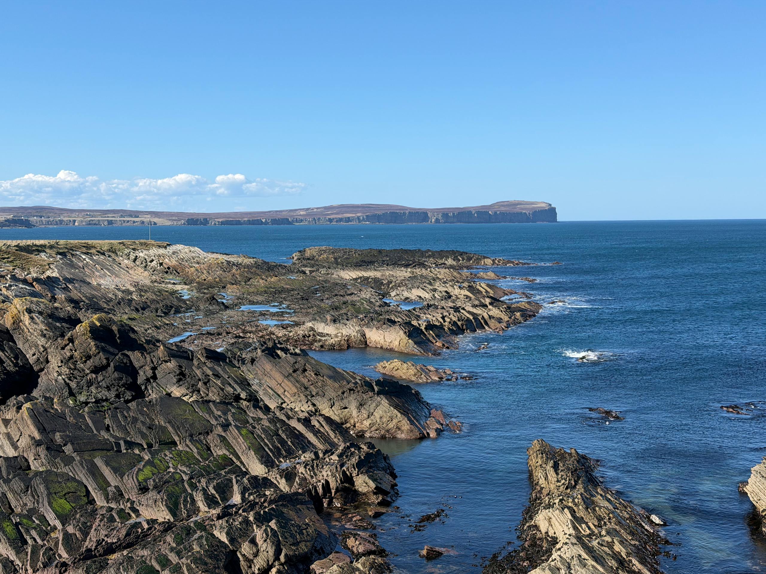 Stunning seascape along the rugged coast of the Orkney Islands, Scotland, under a clear blue sky.